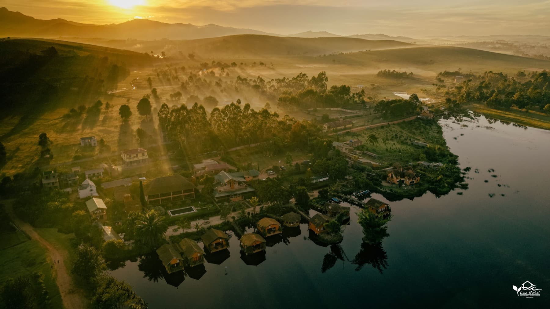Lever de soleil sur le Lac Hôtel Sahambavy, les bungalows sur pilotis et les collines, vus au drone